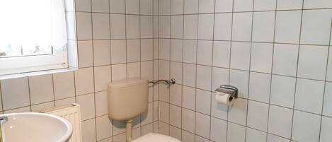A small, tiled bathroom with a toilet, a bidet, and a window.