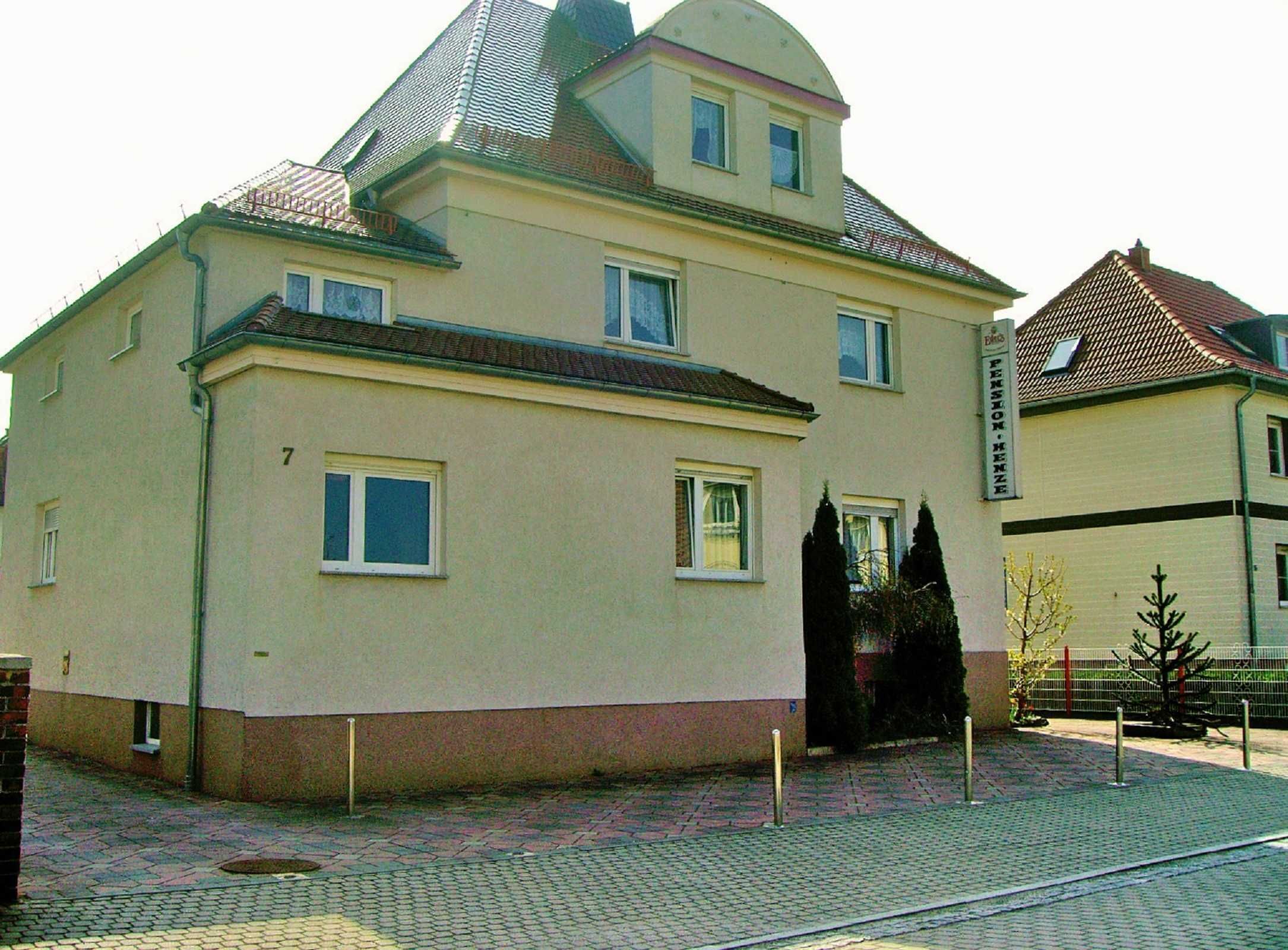 A two-story building with a flat roof, a small balcony on the second floor, and a sign indicating it is a pension home.