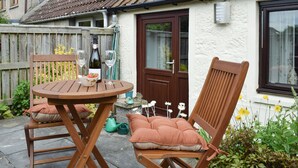 A patio with a round wooden table and two wooden chairs, a bottle of wine, and a bowl of strawberries. - Horseshoe Cottage is cosy and welcoming, perfect for a romantic break. (Freuchie, near Cupar)