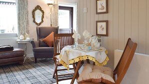 A cozy living room with a fireplace, a dining table set with a lace tablecloth, and framed artwork on the wall. - Horseshoe Cottage is cosy and welcoming, perfect for a romantic break. (Freuchie, near Cupar)