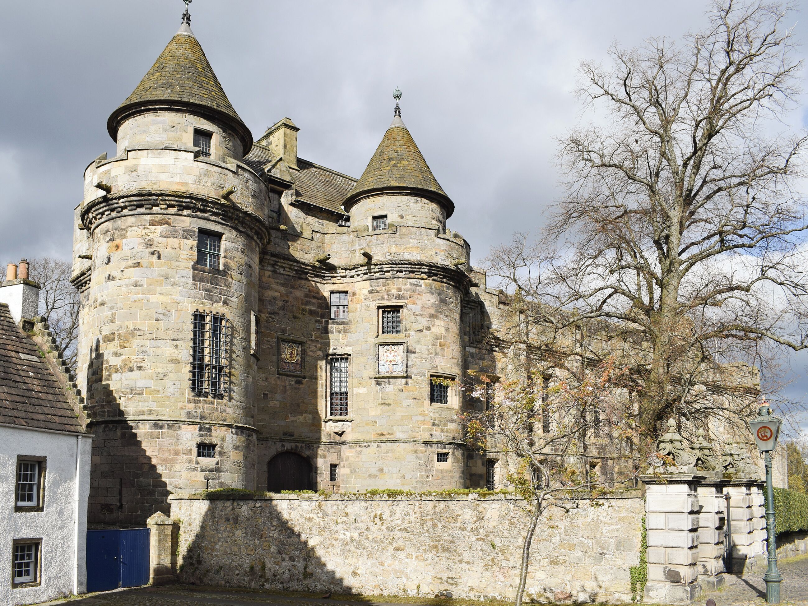 A historic stone castle with multiple towers and a large tree in front.