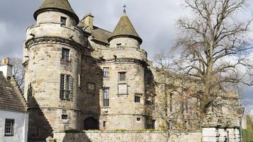 A historic stone castle with multiple towers and a large tree in front.