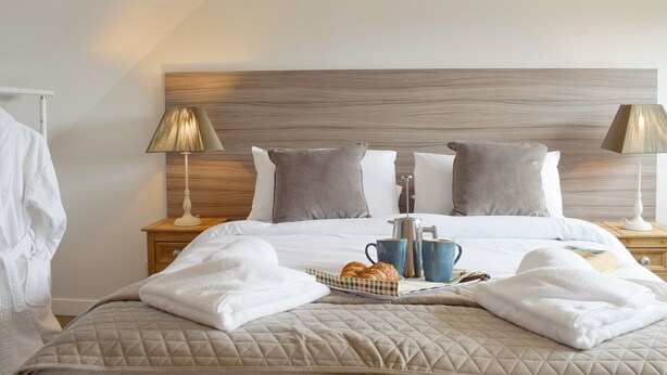 A neatly made bed with a quilted cover, two bedside lamps, a tray with croissants, and a coffee maker on the nightstand. - Horseshoe Cottage is cosy and welcoming, perfect for a romantic break. (Freuchie, near Cupar)