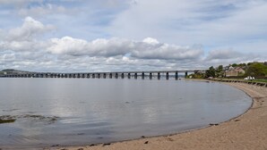 A waterfront with a long pier extending into calm water, a sandy beach, and a town in the background. - Horseshoe Cottage is cosy and welcoming, perfect for a romantic break. (Freuchie, near Cupar)