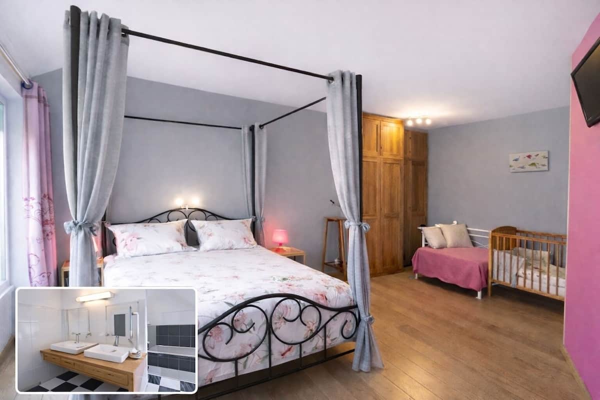 A bedroom with a four-poster bed, a wooden wardrobe, a crib, and a small bedside table with a lamp.
