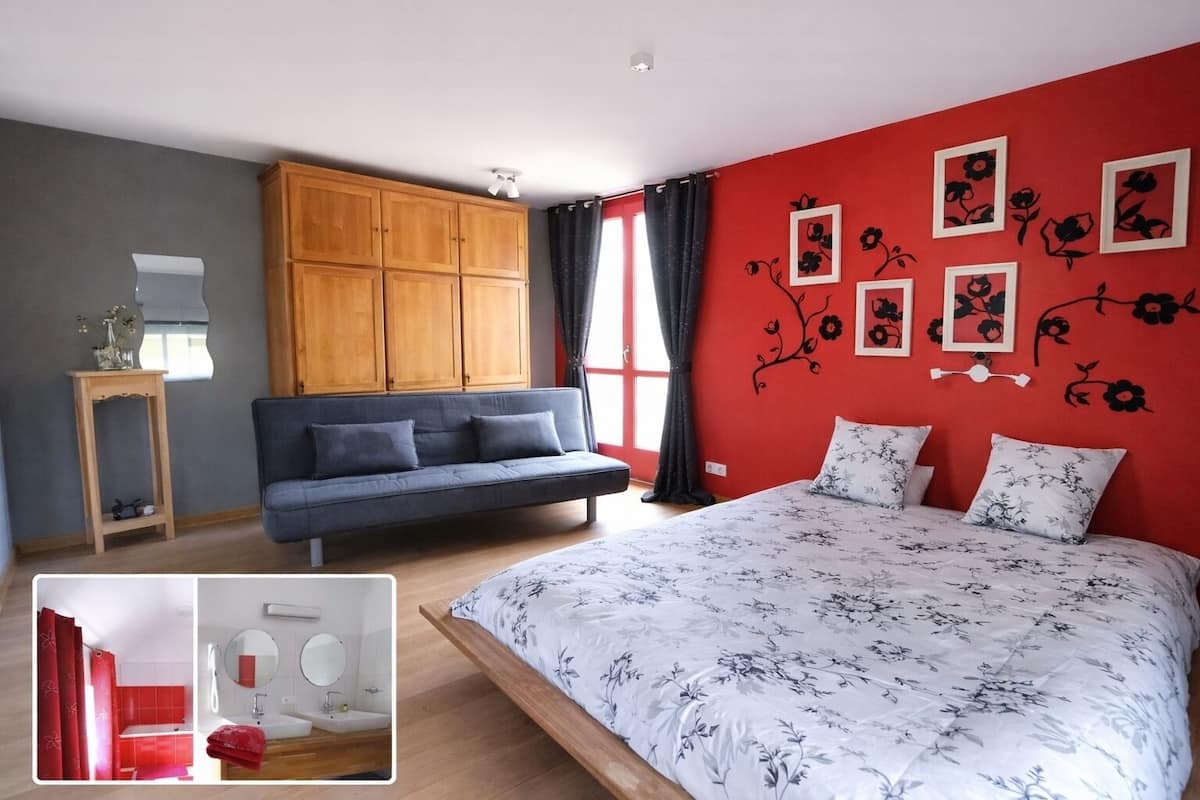 A bedroom with a bed, sofa, wooden wardrobe, and a red wall with floral decorations.