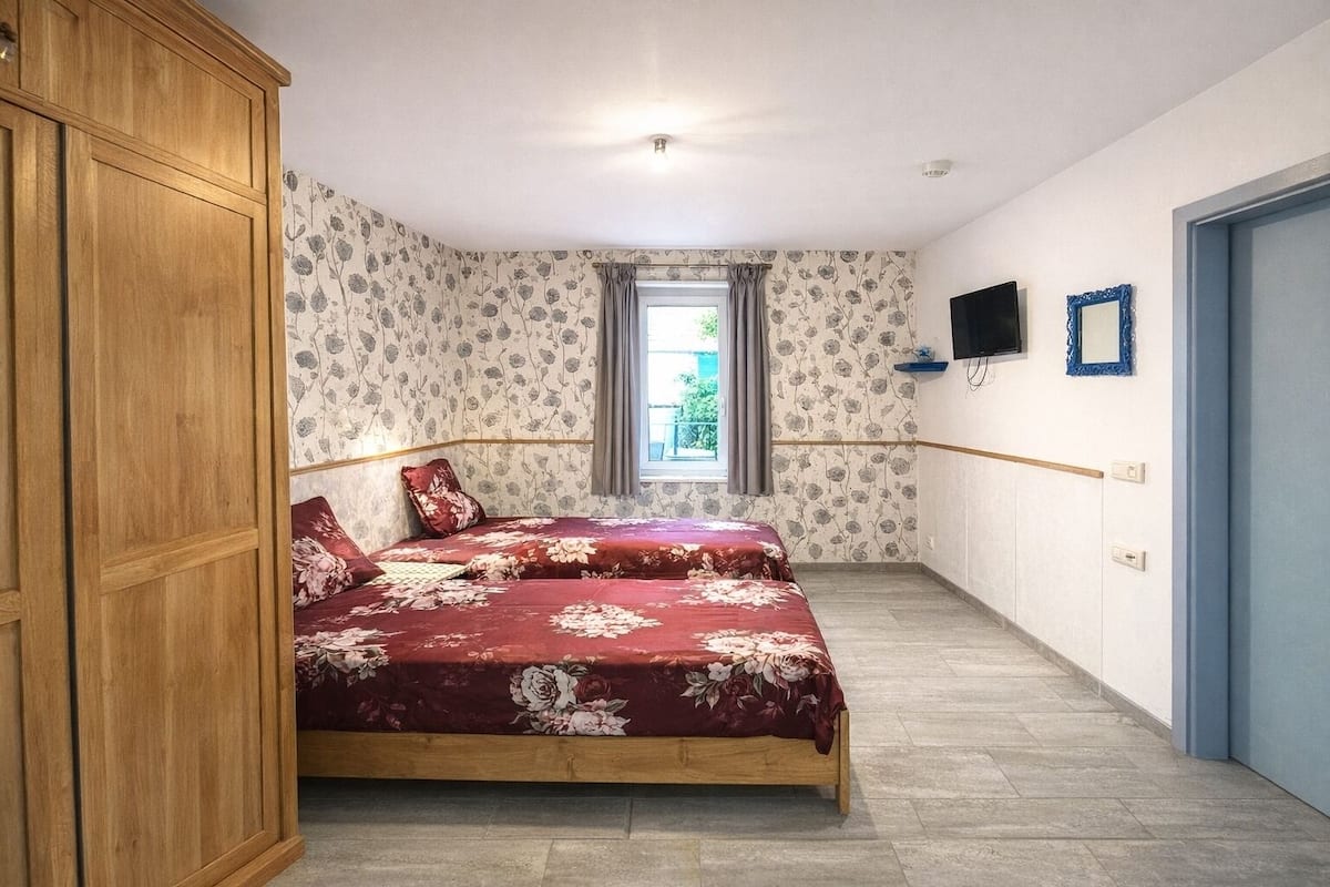 A bedroom with a bed, wardrobe, window, and wall-mounted TV.