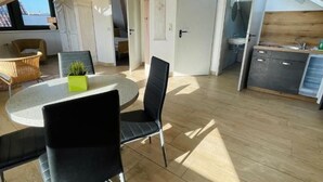 A spacious living area with a round table, black chairs, and a potted plant. There is a kitchen area with a sink and cabinets. - Apartment Beulig-Tietz 2 - Apartment Beulig-Tietz GM 69105 (Graal-Müritz)