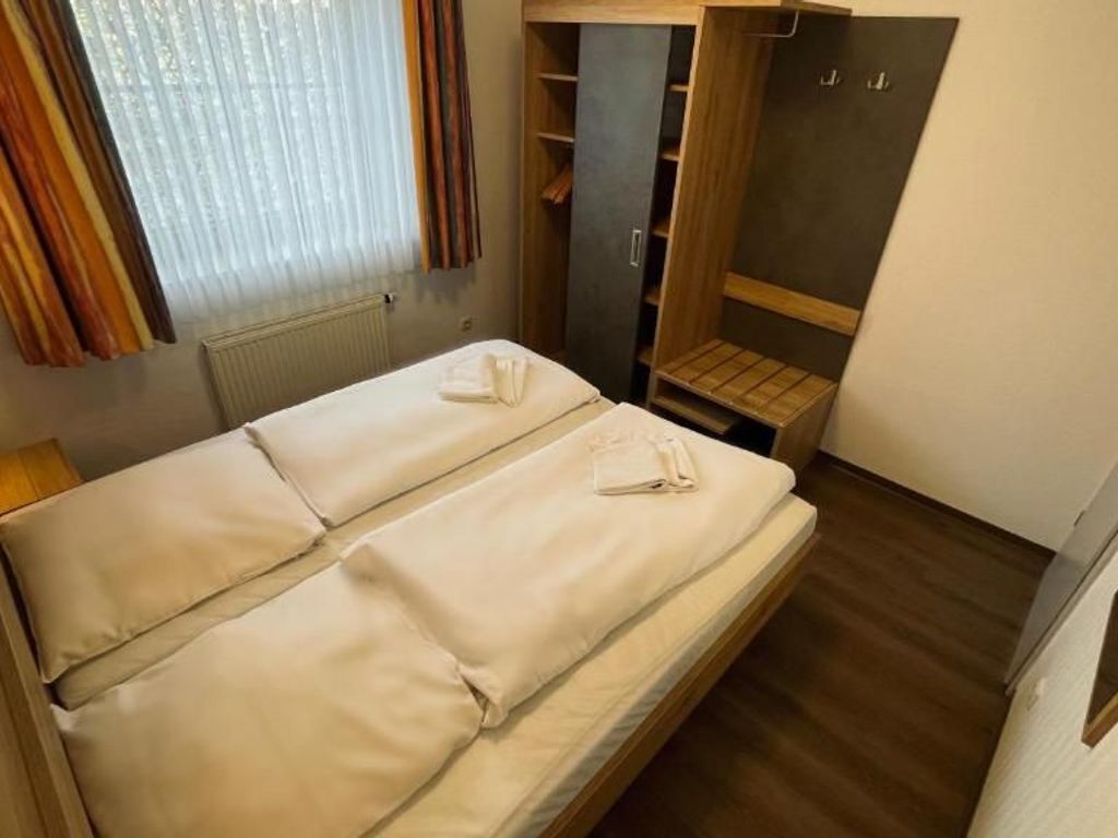 A compact room with a single bed, a built-in wardrobe, and a small seating area.