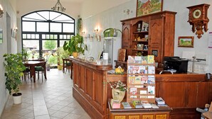 A reception area with a wooden counter, potted plants, a large window, and a wall clock. - Sleeping berth in Heukoje (Box 2) - Hay bunks on the farm (Putbus)
