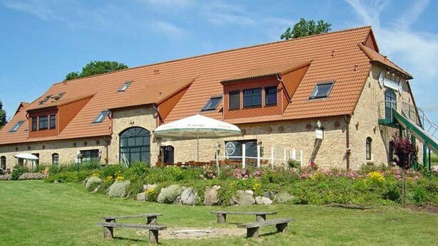 A large building with a sloped roof, a stone facade, and a grassy lawn with picnic tables. - Sleeping berth in Heukoje (Box 2) - Hay bunks on the farm (Putbus)