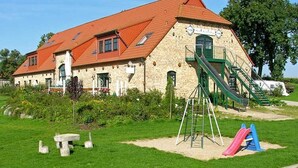 A building with a red roof, a green staircase, and a playground with slides. - Sleeping berth in Heukoje (Box 2) - Hay bunks on the farm (Putbus)