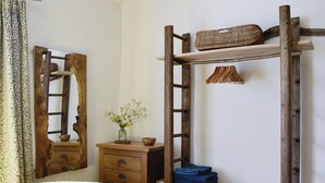Un dormitorio con una cama, cómoda de madera, espejo y estante de madera con una cesta y ropa doblada.