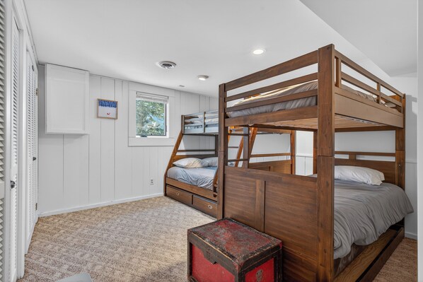 Habitación con literas, paredes blancas, una ventana y un caja roja para guardar objetos.
