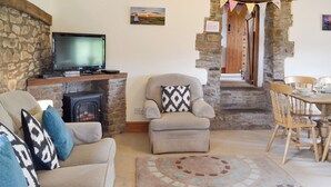 A cozy living room with a fireplace, a television, a sofa, and a dining area with wooden chairs. - Woodland View-UK11826 (Sarnau, near Brecon)