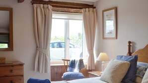 A bedroom with a bed, pillows, a nightstand, a lamp, a chair, a window with curtains, and a wooden headboard. - Woodland View-UK11826 (Sarnau, near Brecon)