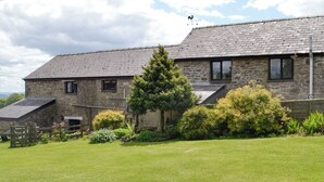 A stone building with a sloped roof, a fenced yard, and a variety of shrubs and flowers. - Woodland View-UK11826 (Sarnau, near Brecon)