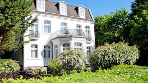 A white building with multiple windows and balconies, surrounded by lush greenery and trees. - 10 double rooms - villa in the Baltic resort Baabe (Baabe)