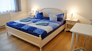 A neatly made bed with blue and white bedding, two bedside tables with lamps, and a white chair in a room with wooden flooring. - 10 double rooms - villa in the Baltic resort Baabe (Baabe)