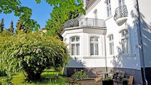 A white building with a balcony and a tree in the foreground. - 10 double rooms - villa in the Baltic resort Baabe (Baabe)