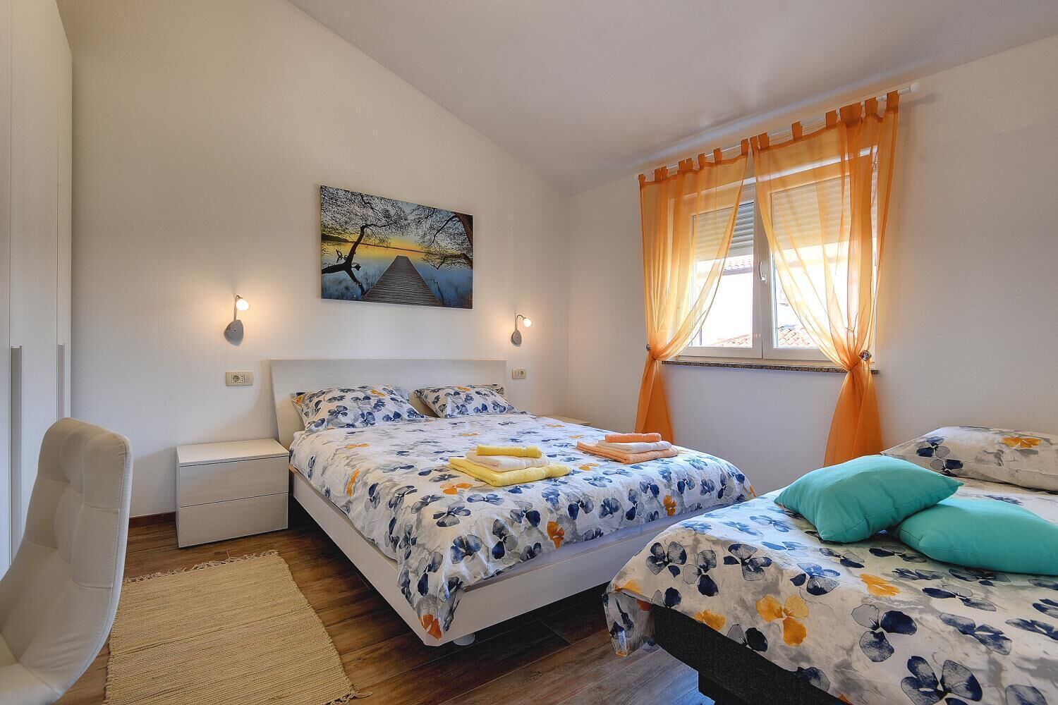 A bedroom with a bed, a chair, a bedside table, a window with curtains, and a painting on the wall.