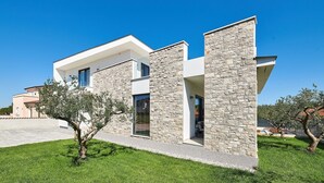 A modern two-story house with a stone facade, large windows, and a well-maintained lawn.