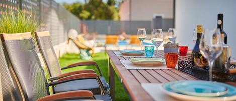 An outdoor dining area with a wooden table set for four, surrounded by chairs.