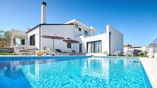 A modern house with a swimming pool, sun loungers, and umbrellas.
