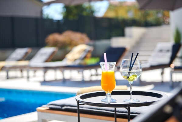 A poolside area with lounge chairs and a table holding two drinks.