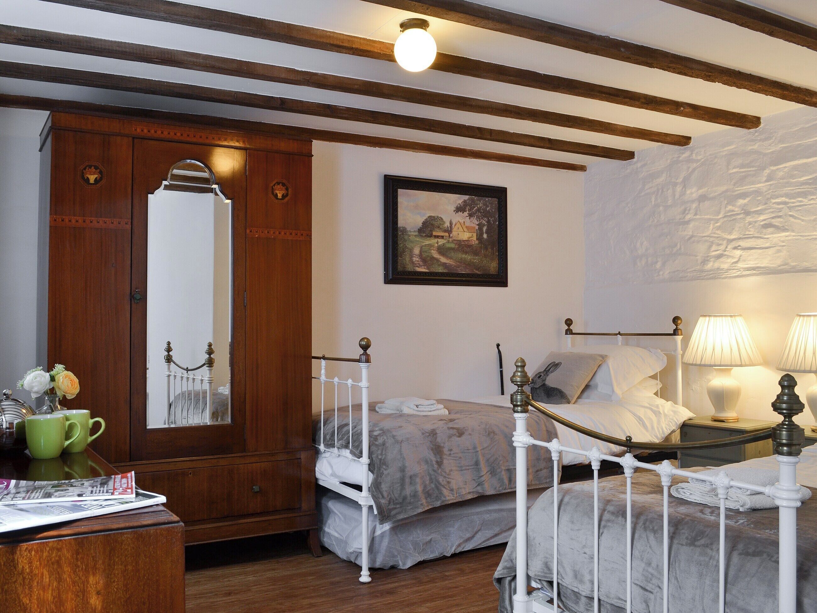 Un dormitorio con un armario de madera, una cama con cabecero de metal blanco, un cuadro en la pared y una lámpara en la mesita de noche.