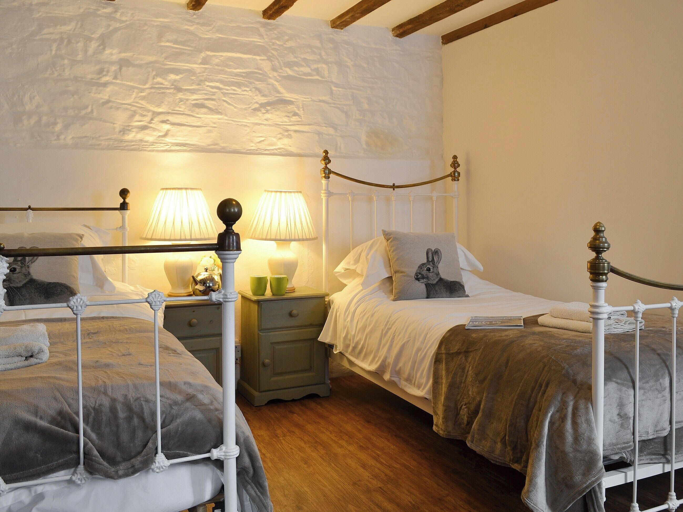 Un dormitorio con dos camas individuales, una mesita de noche con lámparas y una pared de piedra.