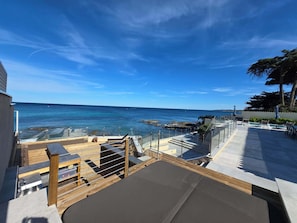 A coastal view from a balcony with a clear sky, a wooden deck, and a pool area.