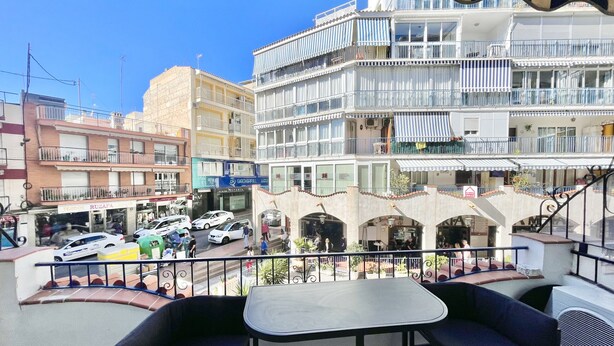 Ein Balkon mit zwei schwarzen Stühlen und einem Tisch, der auf eine Straße mit parkenden Autos und Gebäuden blickt.