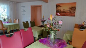 A dining area with tables set for four, chairs, and a vase with flowers on the table.
