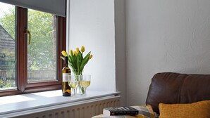 Een raam met uitzicht op bomen, een fles wijn, twee glazen en een boek op een kussen.