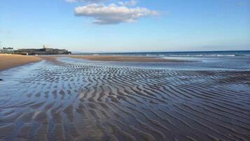 A beach with rippled sand patterns and a distant structure on the left.