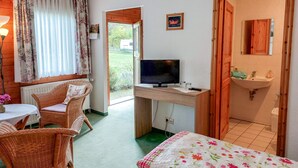 A room with a bed, a desk with a television, wicker chairs, a window with curtains, and a view of the outdoors. - Double room 5 - Rankwitzer Hof (Rankwitz)