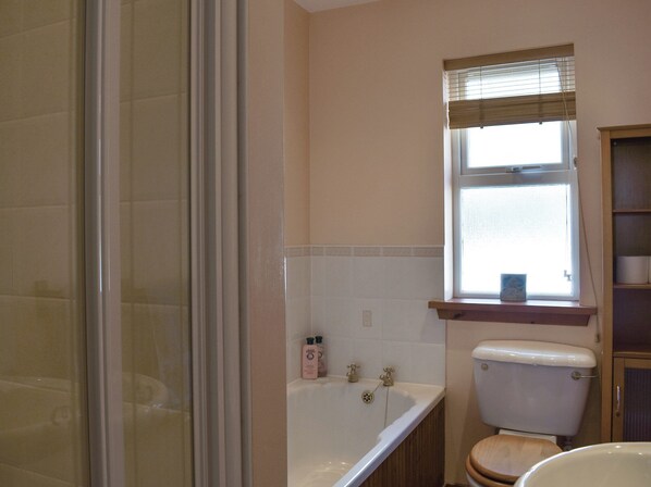A bathroom with a bathtub, toilet, and a window with a shelf above it.