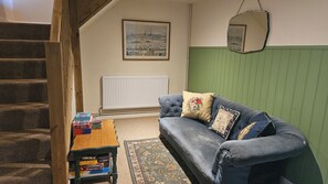 Ein Wohnzimmer mit einer Couch, einem kleinen Tisch mit Gesellschaftsspielen, einer Heizung, einem gerahmten Bild an der Wand und einer Treppe.