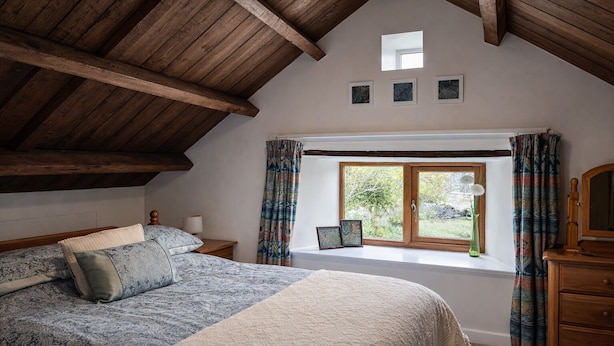 Un dormitorio con una cama grande, un aparador de madera, una ventana con cortinas y un tragaluz.