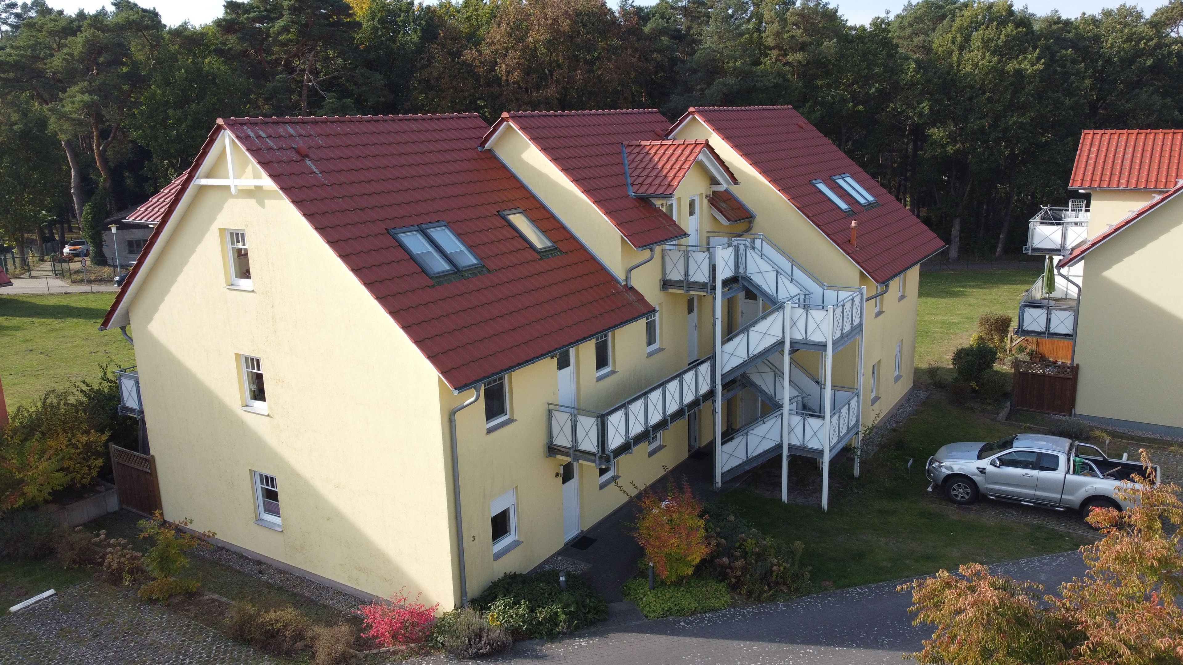 A multi-story building with a red roof, a staircase, and a car parked in the driveway.