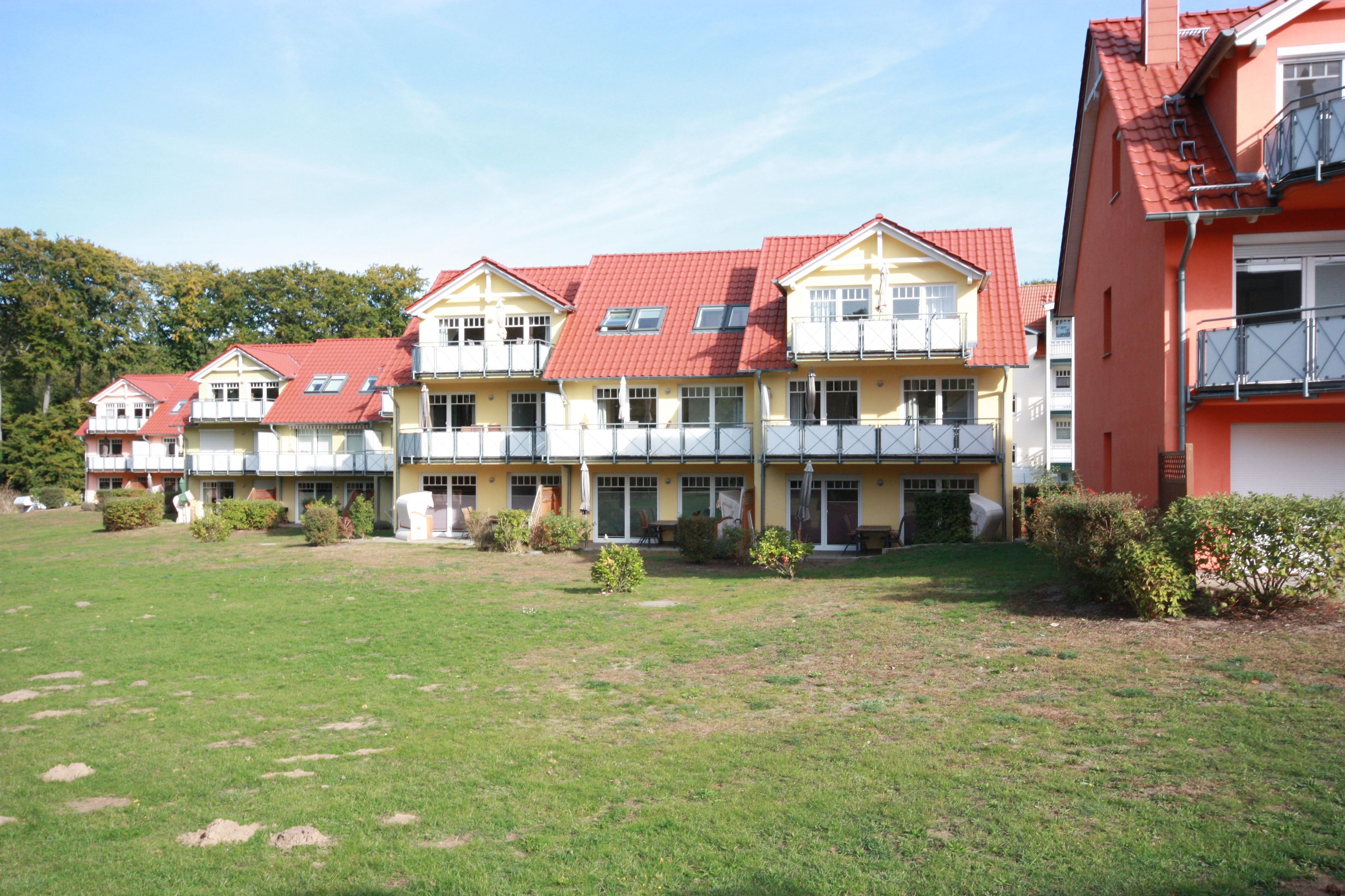 A row of multi-story buildings with balconies, a grassy courtyard, and a clear sky.