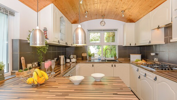 A modern kitchen with wooden ceiling, white cabinets, and a large island with a bowl and fruit bowl.