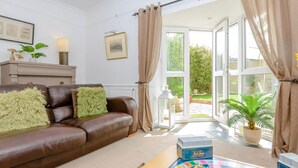 A living room with a brown leather sofa, a coffee table with a board game, and a view of a garden through large windows.