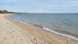 A pebbled beach with gentle waves, a clear sky, and distant boats.