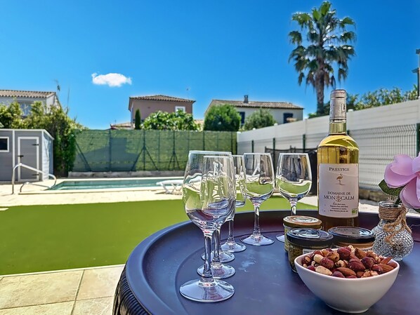 Una mesa con una botella de vino, copas de vino vacías, un cuenco de nueces y una flor decorativa.