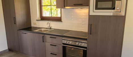 Una cocina con armarios de madera oscura, un microondas de acero inoxidable, un horno empotrado y una ventana con vistas a árboles.