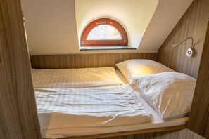 Une petite pièce avec un lit simple, une lucarne et un luminaire fixé au mur.