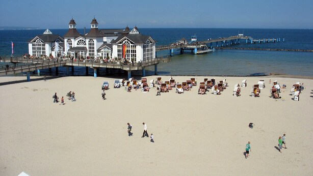 Una playa con un muelle y un edificio con muchas ventanas y una bandera.