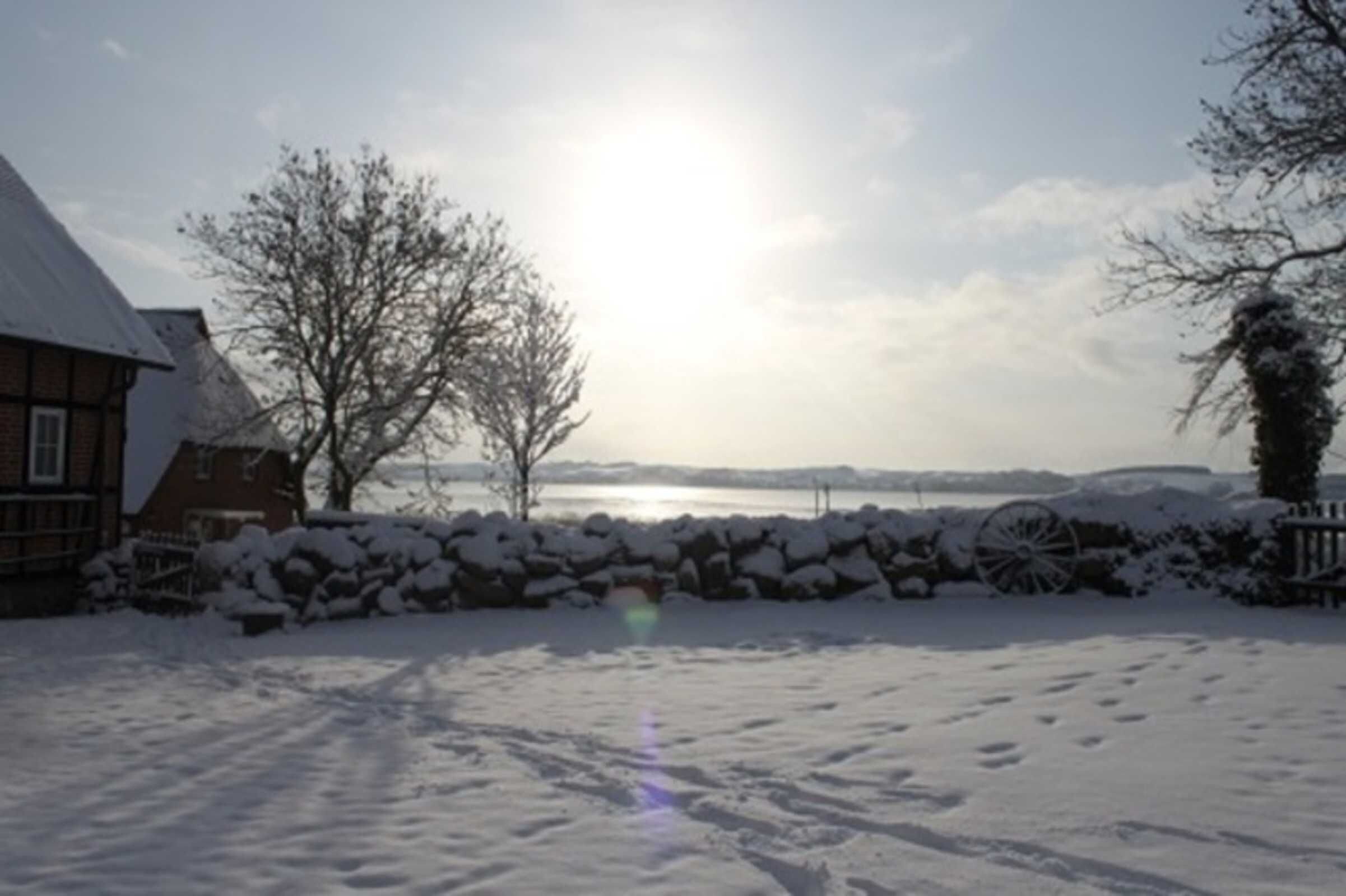 Paesaggio innevato con una casa, un muro in pietra e un corpo d'acqua sullo sfondo.